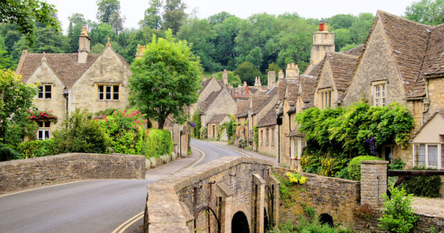A beautiful Cotswolds village is shown, with traditional cottages shown over a bridge surrounded by trees.